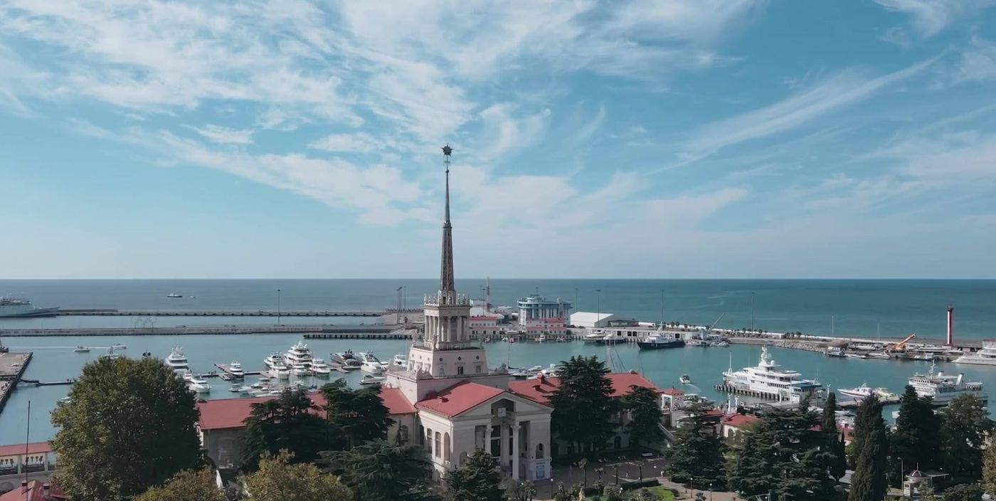 Здание Морского вокзала Сочи со шпилем, за ним гавань с яхтами и море
