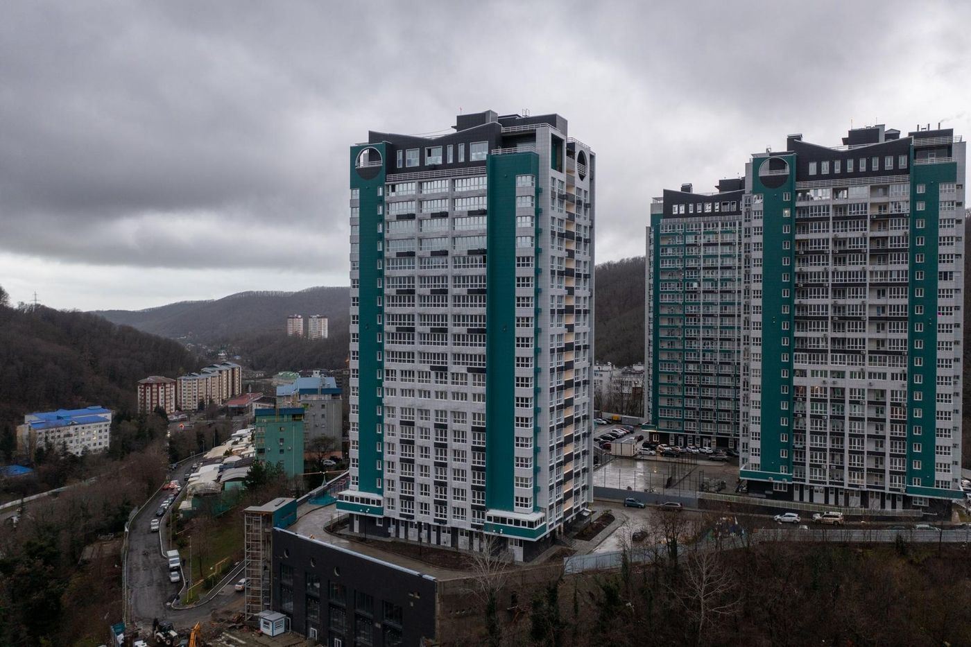 Два 22-этажных дома комплекса в пасмурный день, вокруг холмы и городская застройка