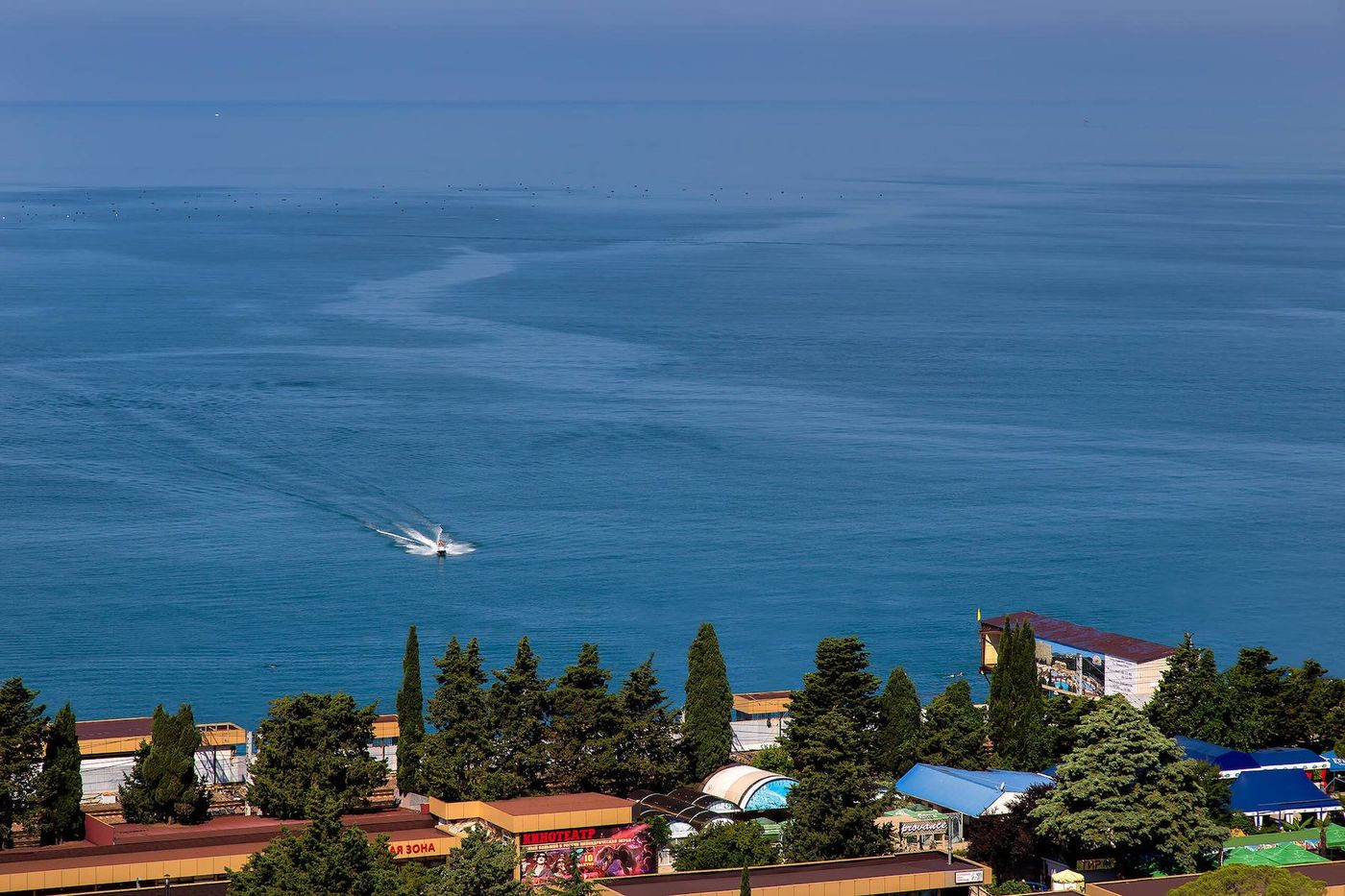 Море с высоты, по воде идёт катер, внизу крыши прибрежных домов и кипарисы