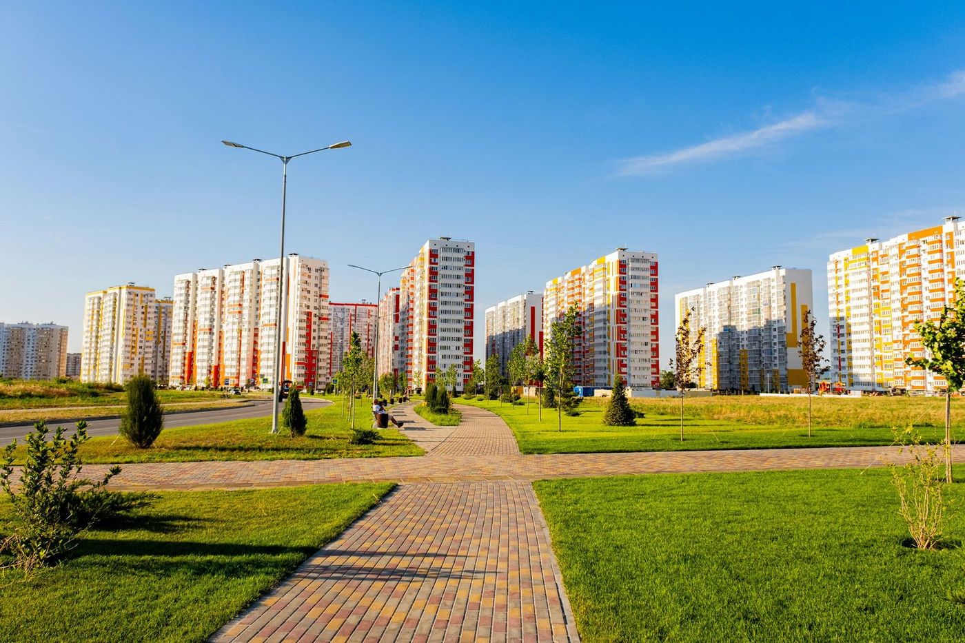 Дорожка из плитки через газон ведёт к рядам многоэтажных домов под голубым небом