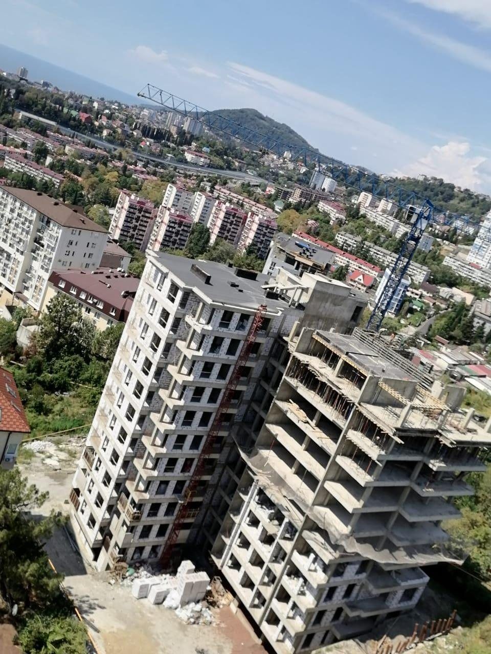 Вид с верхнего этажа строящегося дома на городские кварталы, горы и полосу моря
