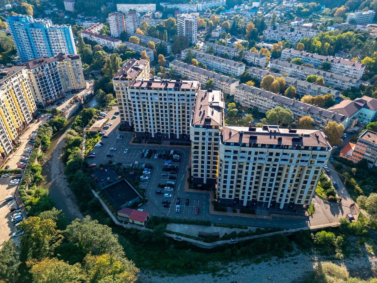 Вид сверху на корпуса комплекса и заполненную машинами парковку во дворе у реки