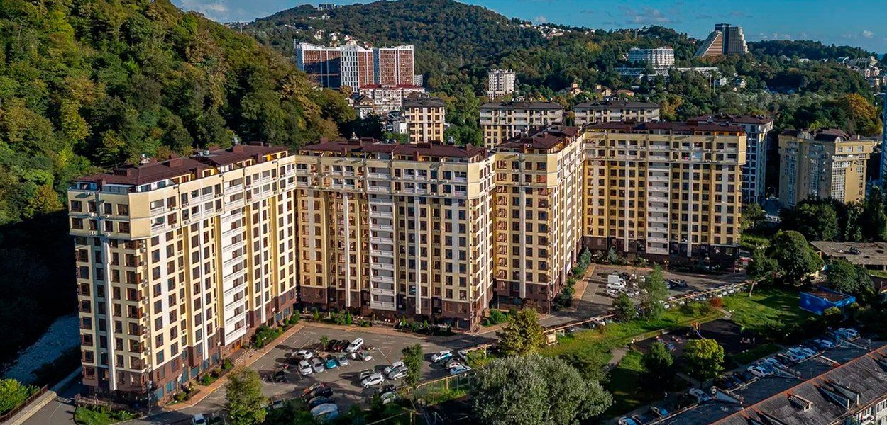 Панорама комплекса сверху: светлые корпуса вдоль склона, парковка и зелень вокруг