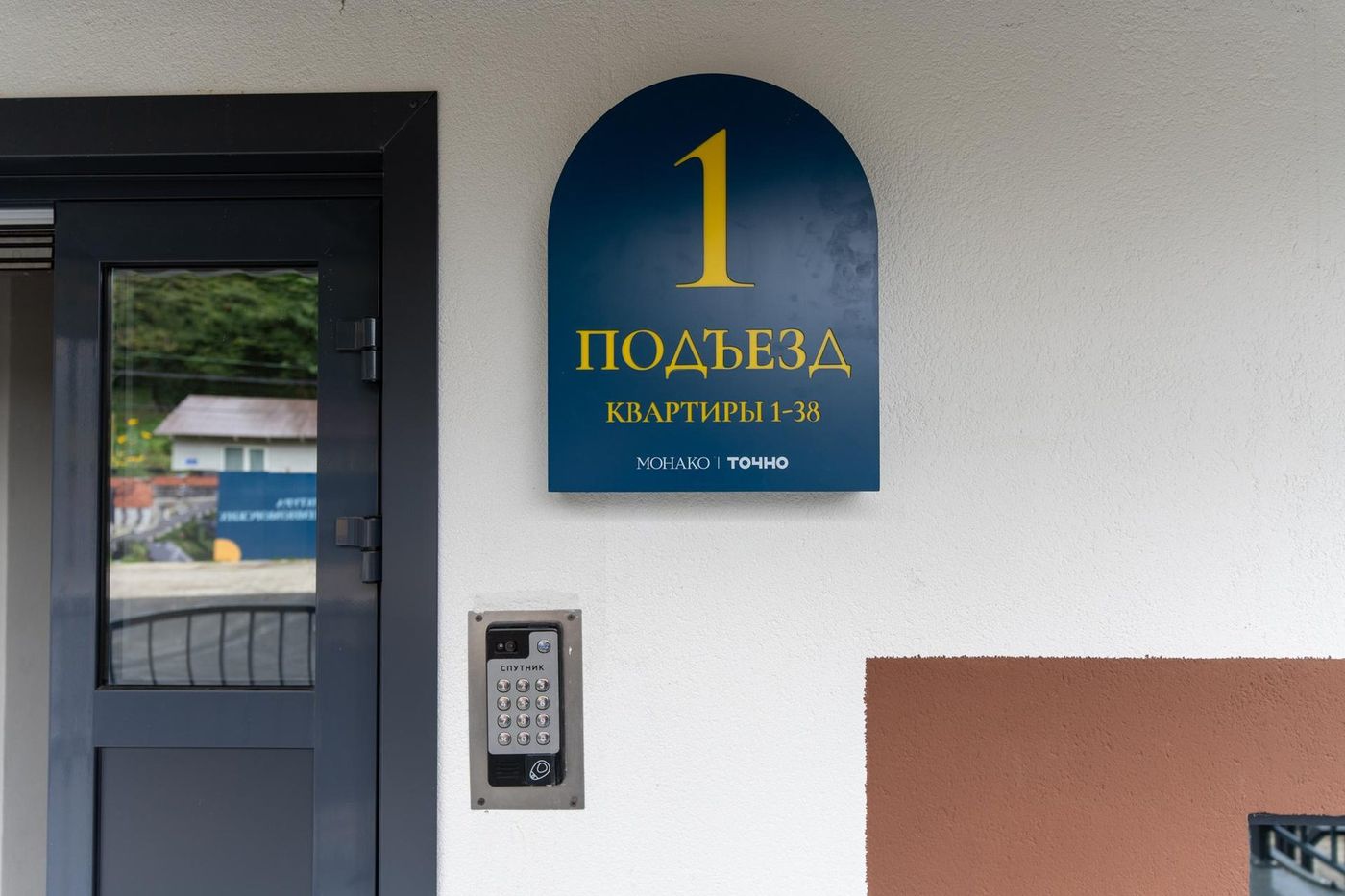 Вход в подъезд: стеклянная дверь, домофон и табличка «1 подъезд» на светлой стене