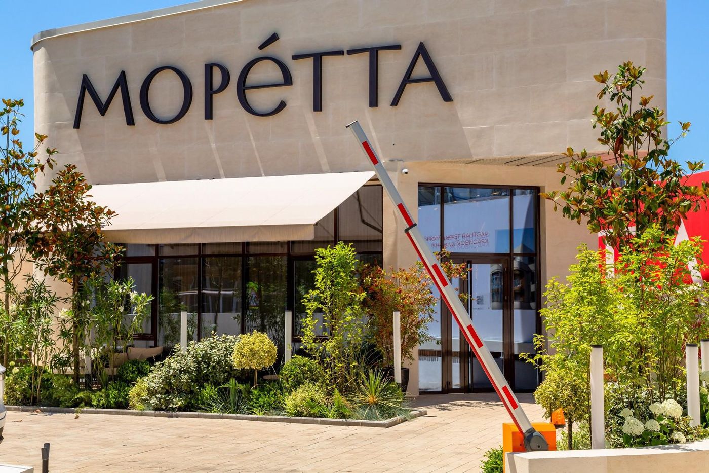 Павильон застройщика с вывеской «МОРЕТТА» на улице Виноградной: светлый фасад, большие окна, цветы и шлагбаум у въезда