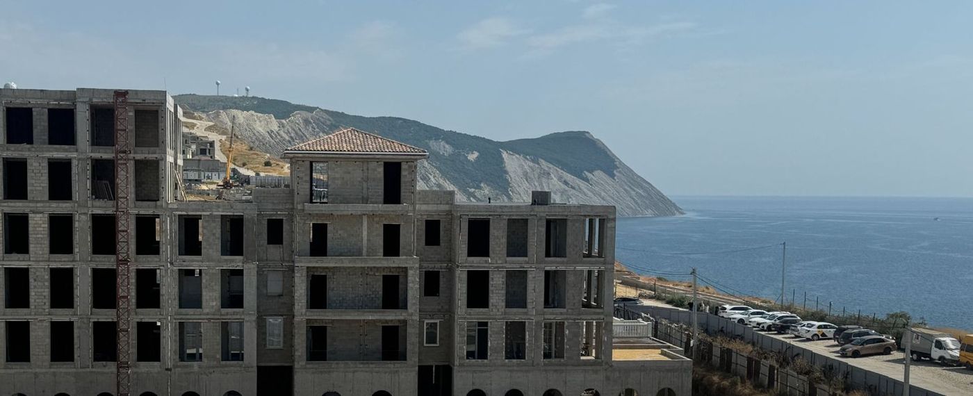 Каркас семиэтажного корпуса на краю берега, справа открытое море и светлые обрывы вдали