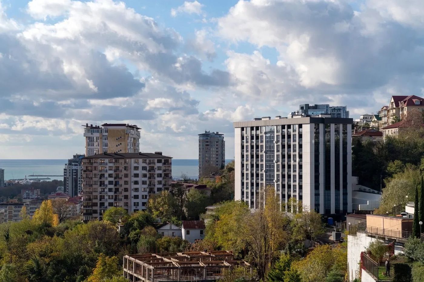 Белый дом среди жилых домов и деревьев на склоне, слева за крышами полоса моря
