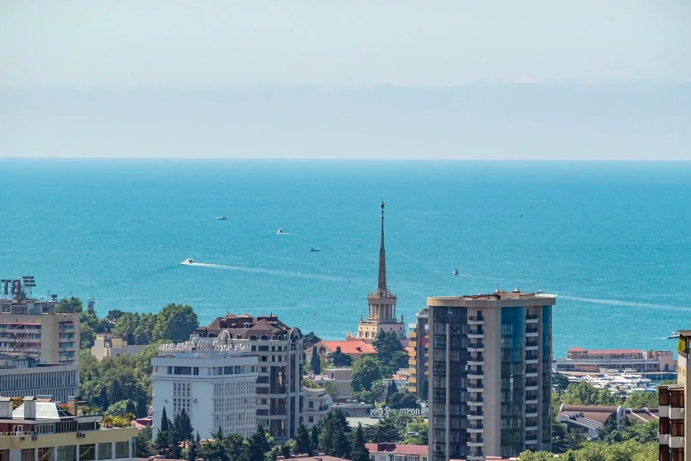 Вид с высоты на центр Сочи: шпиль морского вокзала, дома у побережья и море