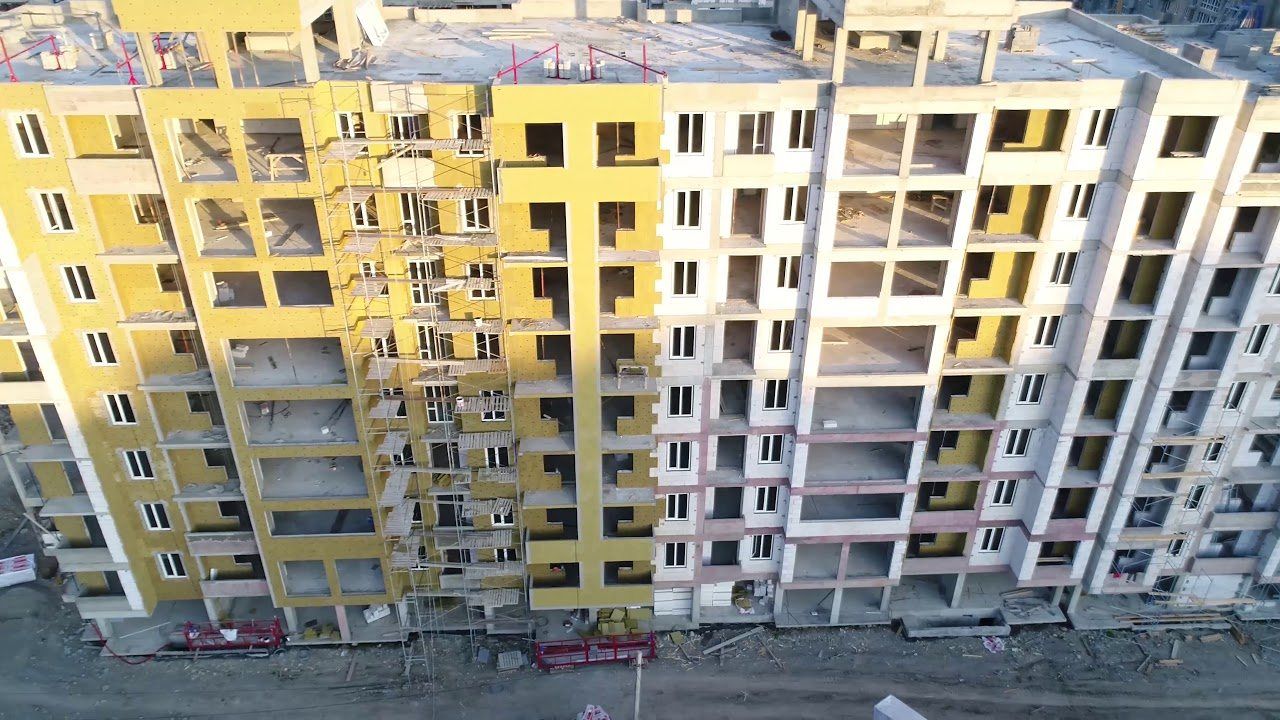 Фасады строящихся десятиэтажных домов с утеплителем и строительными лесами, снятые с высоты