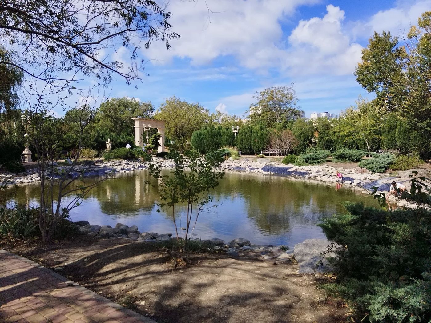 Пруд в парке у собора Андрея Первозванного: вода среди деревьев и кустарников, на дальнем берегу белая беседка