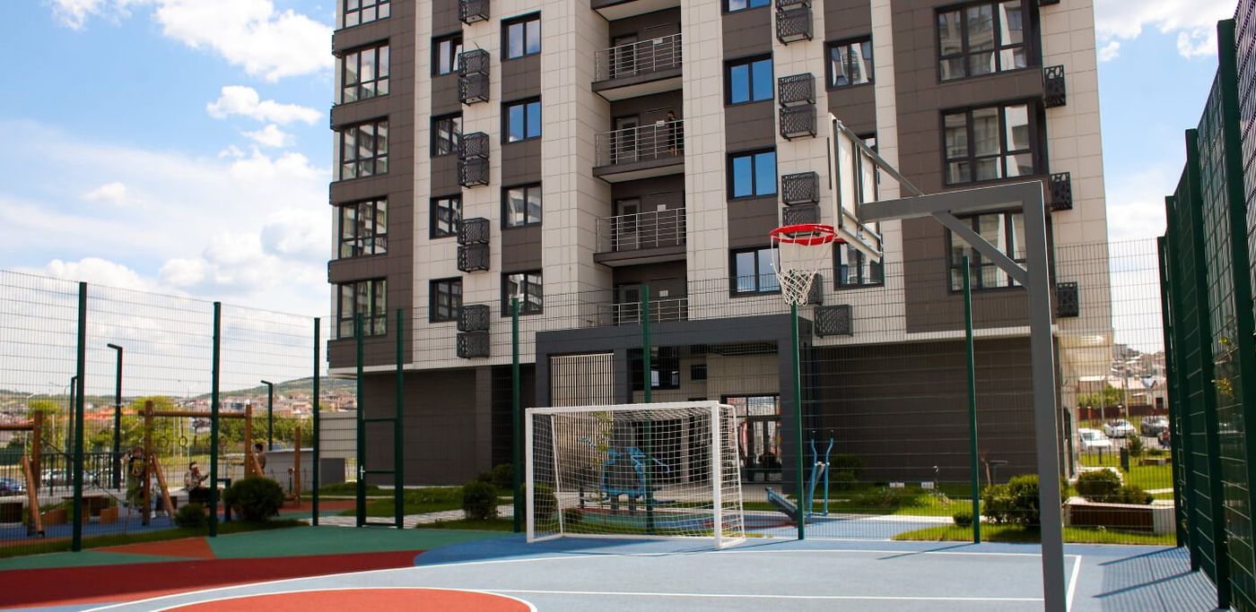 Спортивная площадка во дворе: баскетбольное кольцо, футбольные ворота и сетчатое ограждение на фоне дома