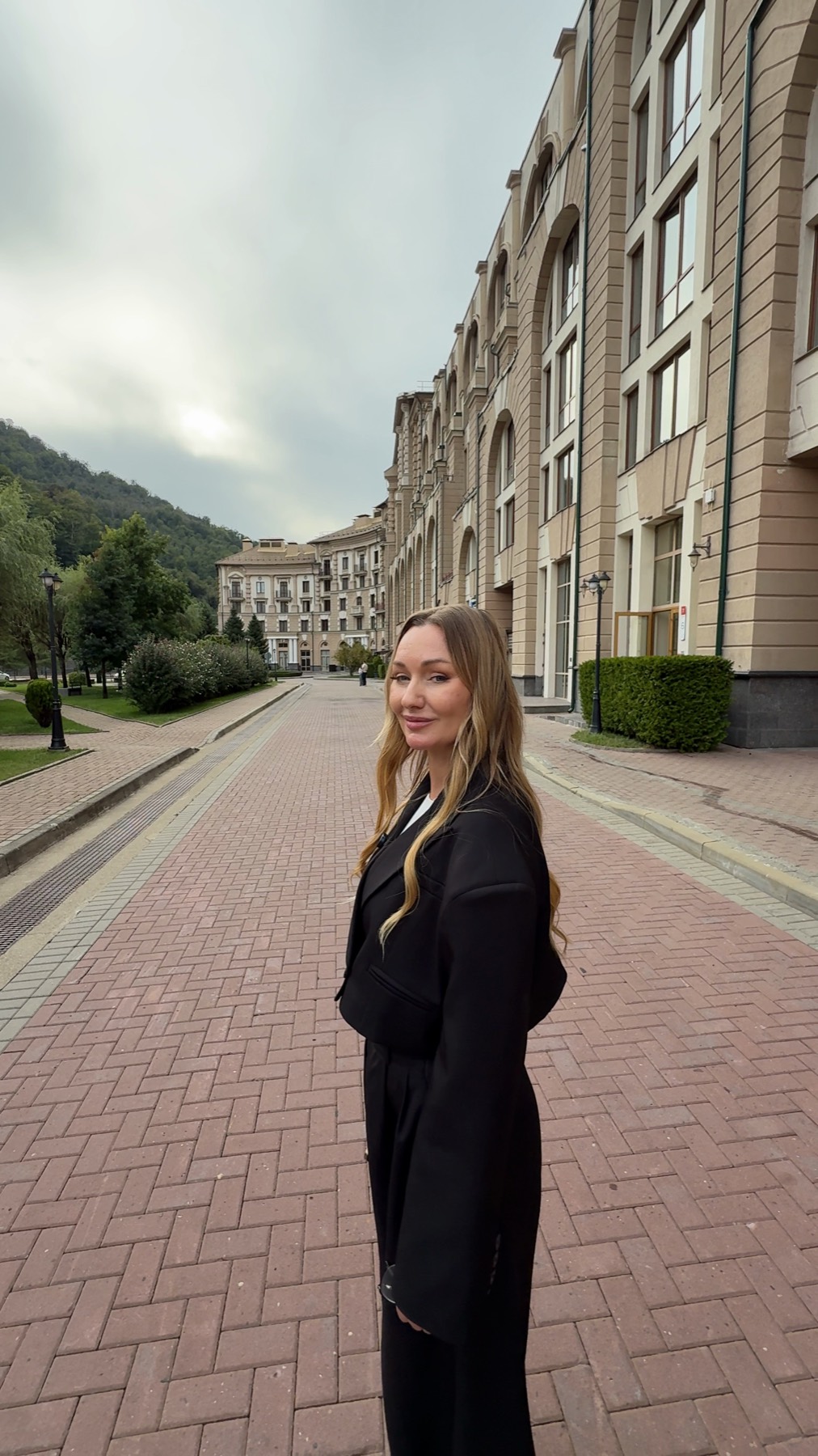 Евгения Гречина на пешеходной улице между аркадными корпусами «Красной Поляны 540», позади зелёная гора