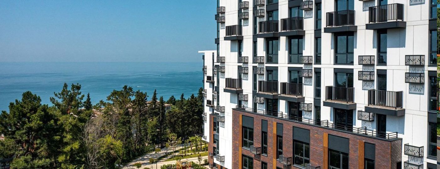 Фасад дома с балконами и решётками, слева за деревьями море