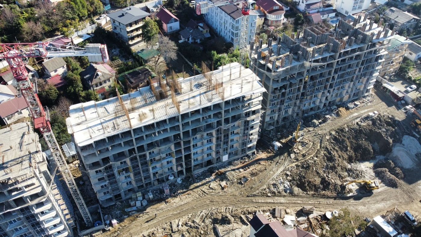 Вид сверху на строящиеся секции комплекса, рядом кран и частные дома