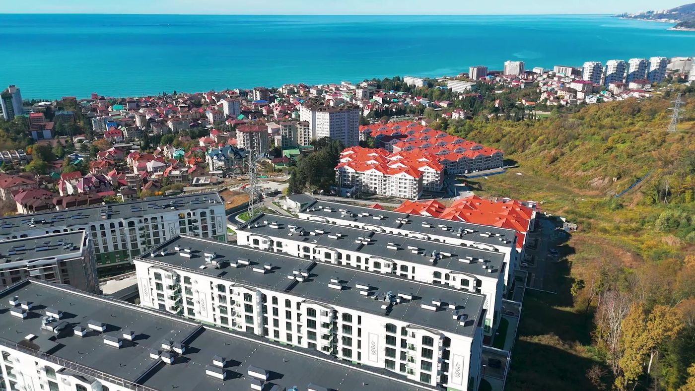 Вид с высоты на крыши домов квартала, соседние дома с красными крышами и море вдоль побережья Адлера