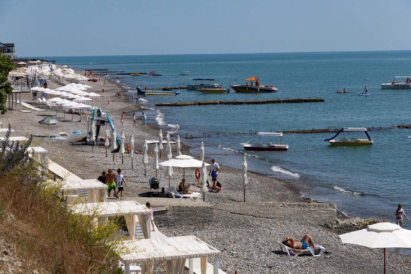 Пляж в Головинке: широкая полоса берега с лежаками и зонтами, в море лодки и катамараны