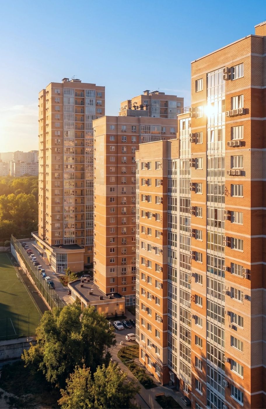 Кирпичные высотки квартала в лучах закатного солнца, внизу деревья и крыши соседних домов