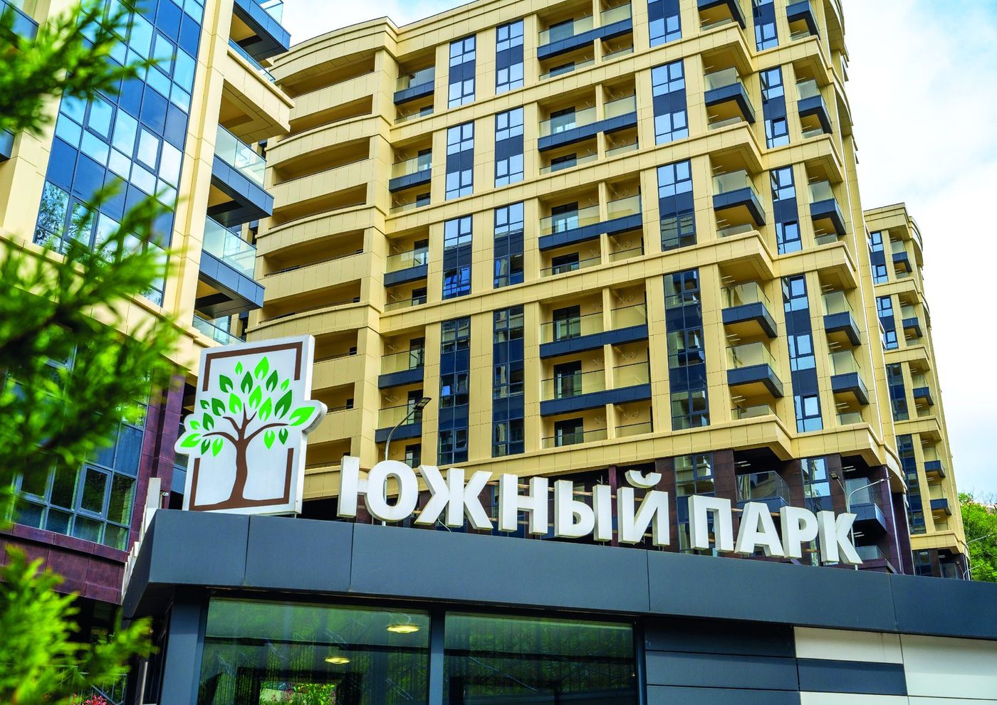Фасад дома с тёмными рамами окон и балконами, над входом вывеска «Южный парк» с деревом